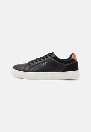 Schwarzer Low-Top-Sneaker mit weißer Sohle, braunem Fersenpatch, schwarzen Schnürsenkeln und kleinem weißen Text an der Seite, auf schlichtem Hintergrund gezeigt.