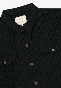 Čierna textúrovaná košeľa na gombíky s dvoma náprsnými vreckami a značkovými kovovými gombíkmi, viditeľným golierom a veľkostnou etiketou XL vo vnútri.