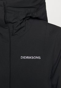 Chaqueta aislante negra con un cuello alto, cuenta con costuras cosidas y el logo bordado "DIDRIKSONS" en blanco. Textura lisa y mate.