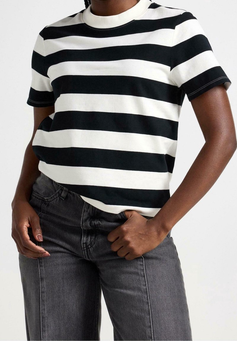 Camiseta de manga corta a rayas en blanco y negro con cuello redondo y un corte relajado, combinada con jeans de color gris oscuro. Tela de algodón suave.