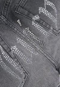 Γκρι ύφασμα τζιν με έντονο σχέδιο από ασημένιες στρας που σχηματίζουν βέλη στην επιφάνεια, αναδεικνύοντας την υφή και τη λεπτομέρεια.