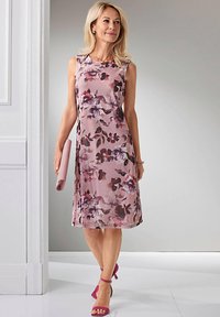 Robe sans manches, longueur genoux, de couleur rose clair avec des motifs floraux sombres ; superposition transparente ; associée à une pochette assortie et des sandales à talons roses.