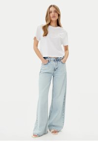 T-shirt bianca corta con il logo "GUESS", abbinata a jeans a gamba larga azzurri. I jeans presentano un vita alta e dettagli strappati.