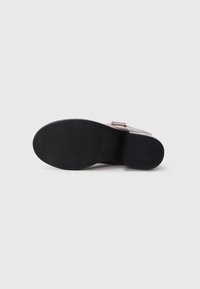 Suela de goma negra de un zapato, con una superficie lisa. El zapato tiene un diseño superior en color burdeos con un detalle de hebilla sencilla.