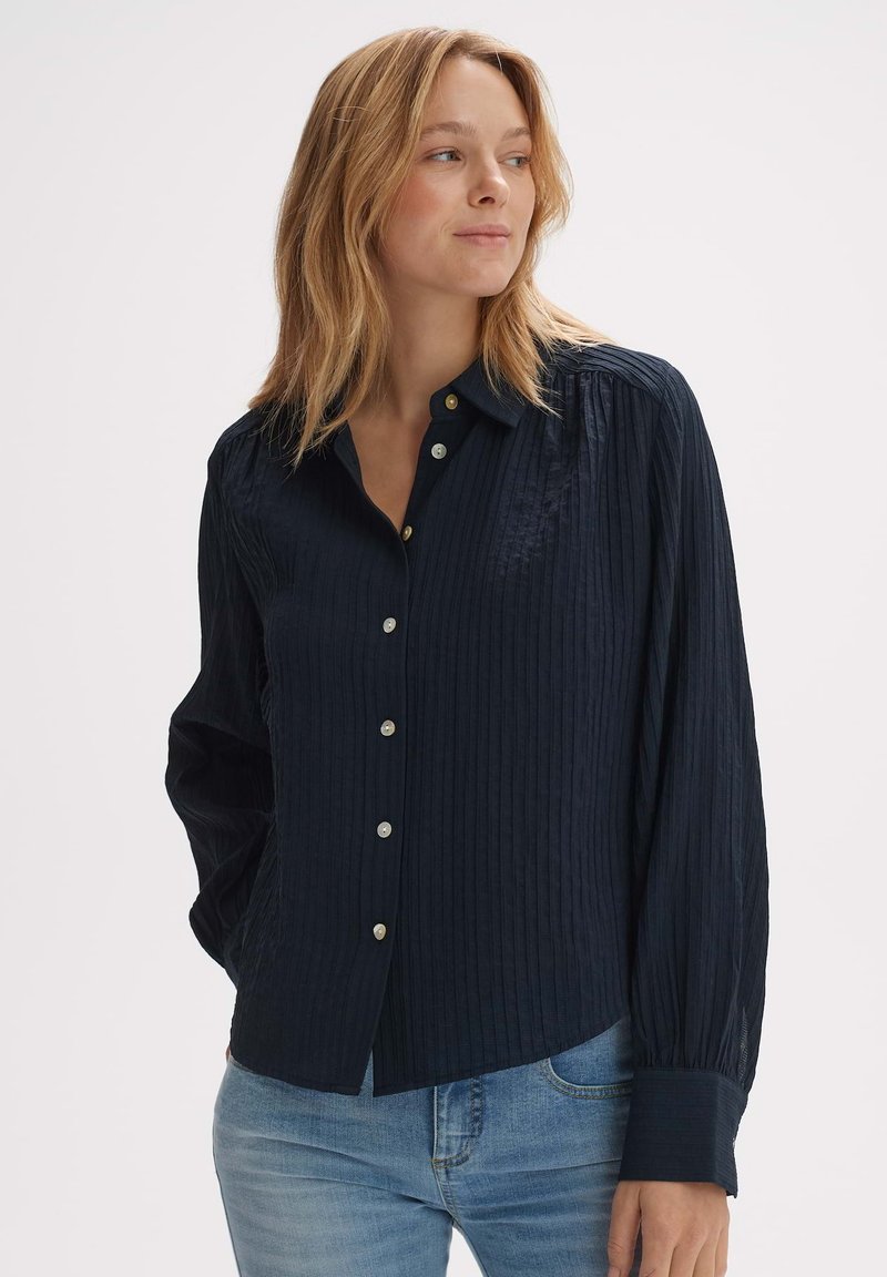 Navy button-up shirt with a textured ribbed pattern, featuring long sleeves and a rounded hem. Buttons are metallic with a subtle shine.