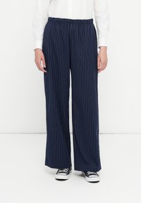 Marineblauwe wijde broek met witte streepjes, elastische tailleband en een gladde stofafwerking. Gecombineerd met zwart-witte sneakers.