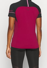 Dopasowany sportowy top w ciemnoróżowym i czarnym kolorze. Krótkie rękawy, materiał odprowadzający wilgoć, kontrastowe panele na ramionach oraz logo na plecach.