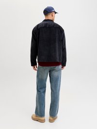 Black corduroy jacket with a relaxed fit, paired with a red sweater, blue jeans, and tan work boots. Back view, minimalistic background.