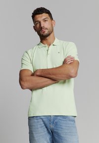 Lichtgroene polo met kraag, korte mouwen en een klein logodetail. Draagt bij lichte blauwe denim jeans.