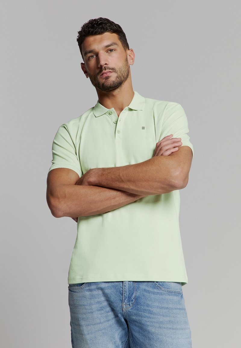 Lichtgroene polo met kraag, korte mouwen en een klein logodetail. Draagt bij lichte blauwe denim jeans.