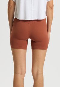 Pantalones cortos deportivos de color óxido, hechos de un material elástico con un diseño ajustado; cuentan con una textura suave y una costura en forma de V en la parte trasera.