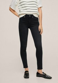 Jeans skinny negros hechos de denim, con un diseño clásico de cinco bolsillos, cintura alta y silueta ajustada, combinados con un suéter de rayas.