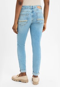 Lichtblauwe skinny jeans met een gladde textuur, voorzien van twee achterzakken en een leren tailleband patch. Opgerolde boorden en casual schoenen.