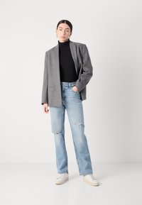 Grå ullblazer over en svart turtleneck, kombinert med lyseblå, ripped jeans og hvite sneakers. Blazeren har strukturerte skuldre.