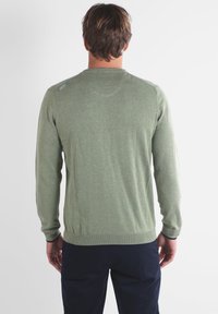 Pull en maille verte à manches longues, avec des poignets et un ourlet côtelés, présentant une texture subtile et un détail de logo sur l'épaule.