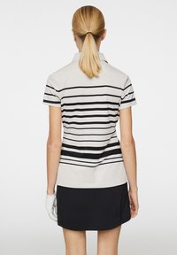 Koszulka polo do golfa z krótkim rękawem w jasnoszarym kolorze z czarnymi poziomymi paskami, w połączeniu z czarną spódnicą. Posiada klasyczny kołnierzyk oraz rękawiczkę.