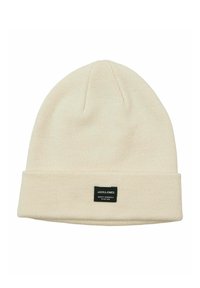 Cappello beanie crema realizzato in tessuto a maglia, con risvolto e un'etichetta nera con testo bianco sul fronte. Texture liscia.