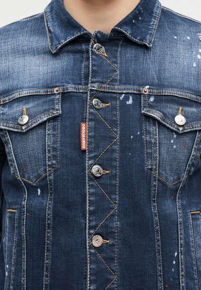 Veste en denim bleu foncé avec boutons en métal, coutures jaunes, deux poches poitrine et une étiquette de marque DSQUARED2 rouge à l'avant.