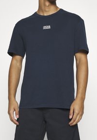 Marinblå bomulls t-shirt med korta ärmar, rund halsringning och vit "JACK & JONES"-logotyp på bröstet. Slät textur, avslappnad passform.