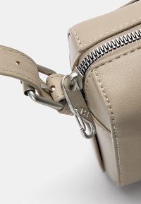 Sac en simili cuir beige avec une fermeture éclair en métal et des éléments en argent, comprenant une attache clip et des détails de couture visibles.
