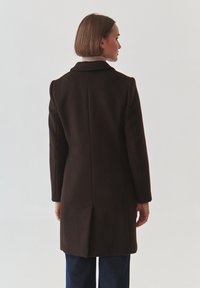 Bruine wollen jas met een gestructureerde silhouet, enkelgeknoopte ontwerp en een notch-kraag. Beschikt over schoudervullingen en zijsplitten.