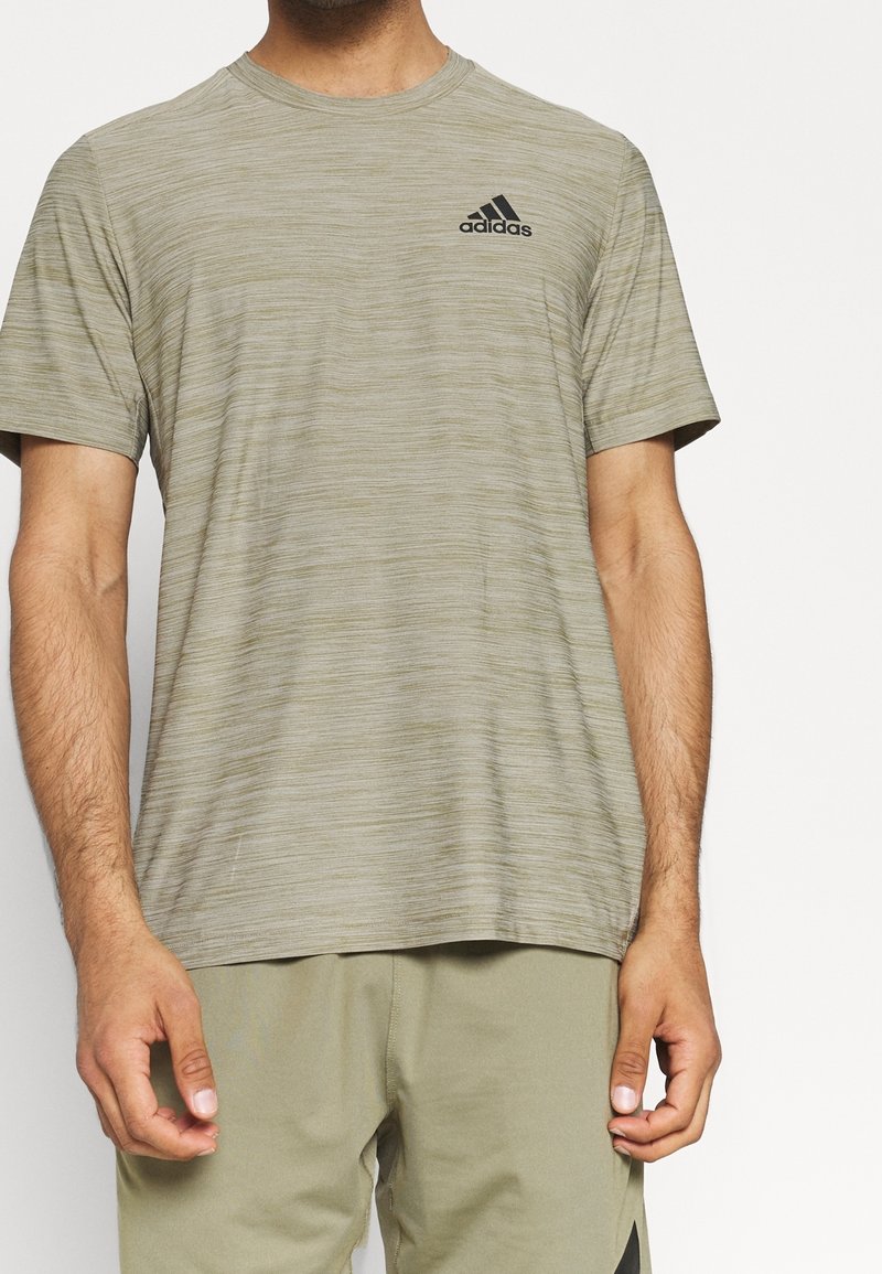 Vihreä oliivinvärinen urheilupaita, joka on valmistettu kevyestä, teksturoidusta kankaasta. Paitassa on lyhyet hihat ja musta Adidas-logo rinnassa.