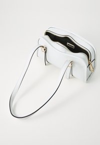 Sac à main en cuir blanc avec des bords noirs, fermeture à double zip, poches intérieures et courtes poignées avec des accents en métal doré.