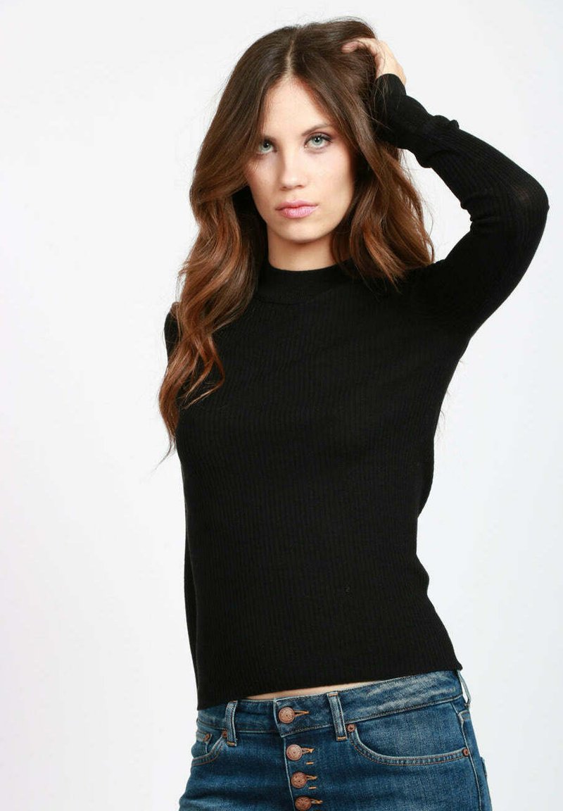 Maglione lungo a maniche nere con coste, colletto alto, silhouette aderente e texture morbida, abbinato a jeans in denim blu e dettagli con bottoni.