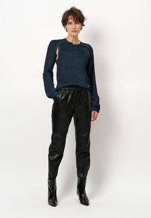 Marineblauwe gebreide trui met uitsparingen op de schouders, gecombineerd met zwarte leren broeken en glanzende zwarte laarzen. Eenvoudige ketting als accent.