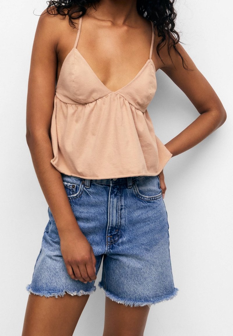 Top sin mangas de color rosa claro con escote en V y cintura fruncida, combinado con pantalones cortos de mezclilla azul de talle alto con dobladillos deshilachados.