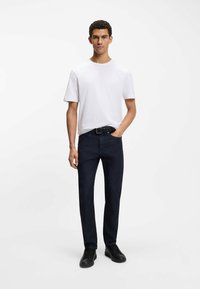 Biała koszulka z krótkim rękawem, ciemnoniebieskie jeansy i czarne trampki; klasyczny krój o gładkiej fakturze i minimalistycznym designie.