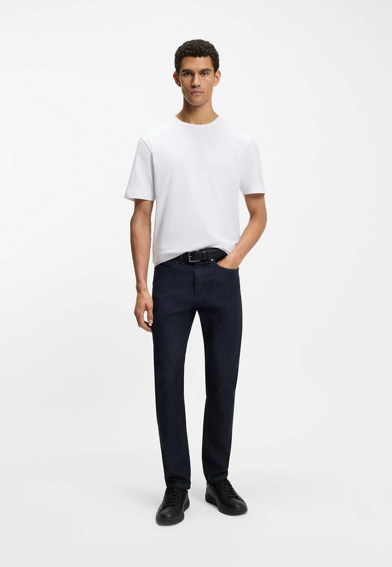 Biała koszulka z krótkim rękawem, ciemnoniebieskie jeansy i czarne trampki; klasyczny krój o gładkiej fakturze i minimalistycznym designie.