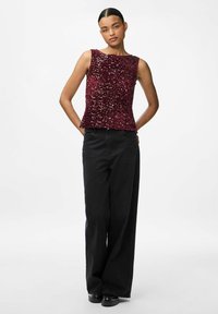 Top en sequins bourgogne avec un design sans manches, un corsage ajusté et un ourlet évasé. Associé à un pantalon large noir et des chaussures noires.