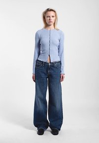 Ljusblå ribbad långärmad topp med knappar framtill och kort design, kombinerad med mörkblå vida jeans med avslappnad passform.