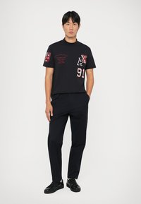 Czarny bawełniany t-shirt z haftowanymi czerwonymi logo, krótkie rękawy i okrągły dekolt. Połączony z czarnymi spodniami i czarnymi butami sportowymi.