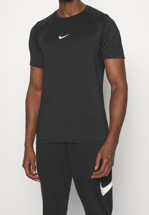 Mężczyzna noszący dopasowaną czarną koszulkę Nike z krótkim rękawem z białym logo oraz czarne spodnie z białym znakiem Nike na lewym udzie.