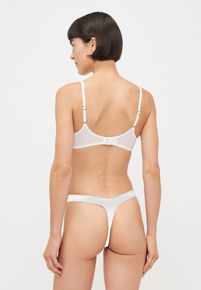Witte lingerieset met een beha met gegolfde rand en verstelbare bandjes, en een bijpassende string. Zacht materiaal met een gladde afwerking.