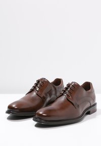 Chaussures de ville en cuir marron avec une finition lisse, design classique à lacets, bout arrondi et détails de couture subtils. Talon bas.