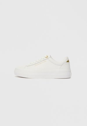 Low-top white sneaker with gold accents, textured upper, white laces, and "Tommy Hilfiger" branding on the side.