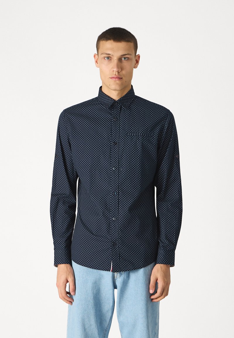 Camisa navy con botones, estampado de lunares blancos, de manga larga, con cuello y un bolsillo en el pecho, hecha de una tela suave. Corte holgado.