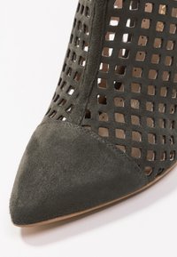 But ze spiczastym czubkiem wykonany z ciemnoszarego zamszu o otwartym wzorze kratki. Charakteryzuje się gładką fakturą i średniej wysokości obcasem, co zwiększa przewiewność.