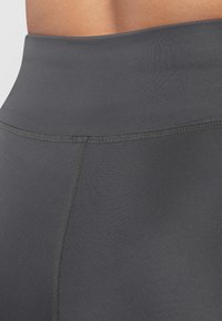 Leggings neri a vita alta realizzati in tessuto elastico, con una texture liscia e cuciture rinforzate lungo le giunture.