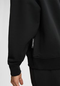 Felpa nera realizzata in tessuto morbido, con polsini e orlo a costine, e un'etichetta tessuta sul lato con la dicitura "STRELLSON."