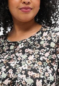 Μαύρο μπλουζάκι με floral σχέδιο που περιλαμβάνει διασκορπισμένα παστέλ λουλούδια σε ροζ, εκρού και πράσινο. Απαλό ύφασμα με στρογγυλή λαιμόκοψη και κοντά μανίκια.