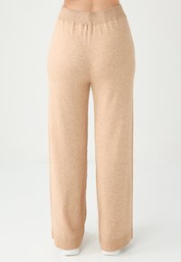 Pantaloni a gamba larga beige realizzati in morbido tessuto a maglia. Presentano una vita elasticizzata e orlo a coste. Texture liscia con vestibilità rilassata.