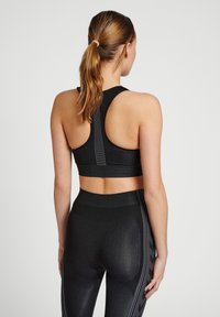 Svart sportbh med racerback-design, texturerat tyg och reflexstripes längs ryggen, i kombination med matchande tights.