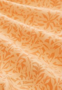 Tissu orange clair avec un motif répétitif de feuilles dans une teinte légèrement plus foncée, présentant une texture lisse et un drapé doux.