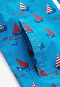 Tissu bleu avec des voiliers rouges et blancs et le texte « Time to Set Sail » répété, équipé d'une poche fendue verticale avec des coutures visibles.