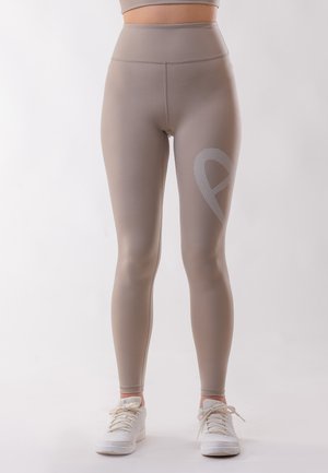 High-waisted, beige workout leggings made from stretchy material with a fitted design and textured, silver logo detail on the left leg.