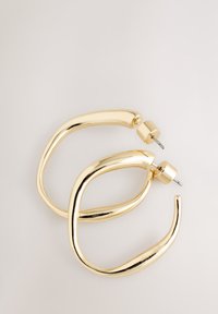 Gold-tone metal hoop earrings with a fluid design, featuring a polished finish and a post-back closure. The shape is elongated and curved.